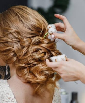 Hair stylist or florist makes the bride a wedding hairstyle with fresh cotton flowers